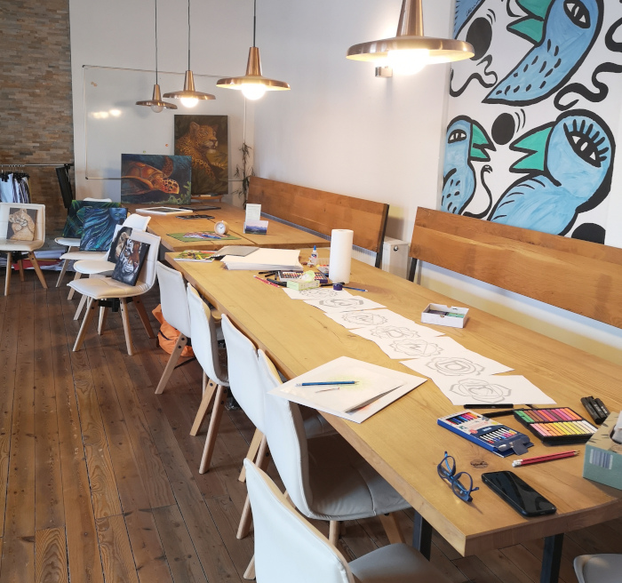 Heller Workshopraum mit langem Holztisch, Zeichenmaterialien und kreativer Atmosphäre